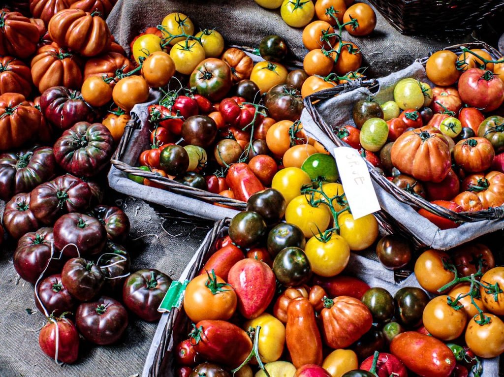 An assortment of fresh, colorful heirloom tomatoes displayed in baskets at an outdoor market, offering a healthy and nutritious option.